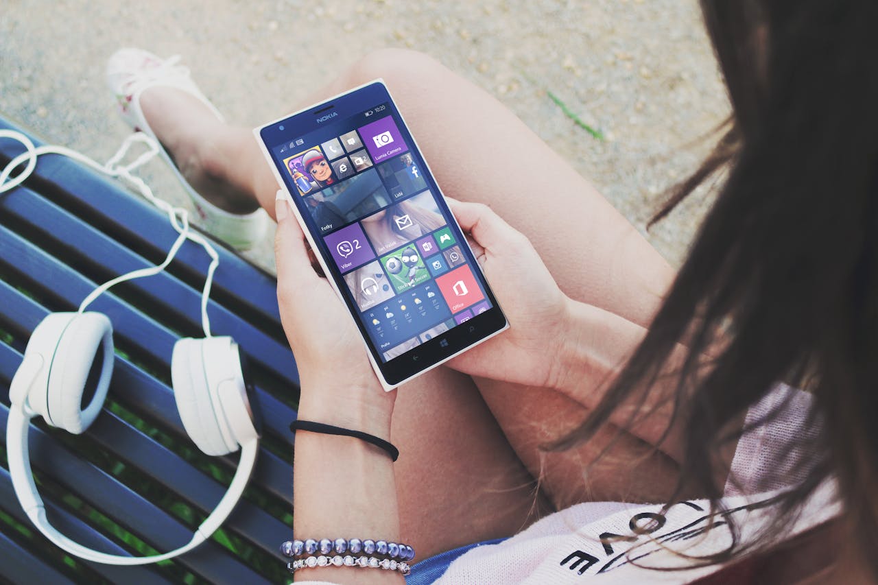 Woman Holding Turned Smartphone While Sitting on Bench Close-up Photography